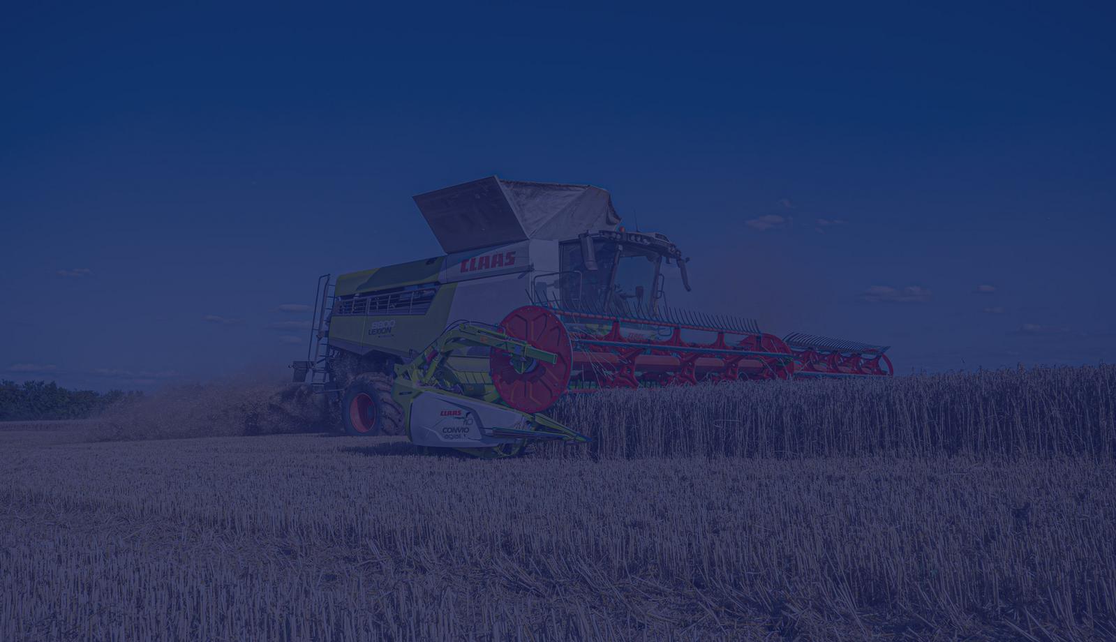 A CLAAS combine harvester working in a golden wheat field under a clear blue sky.